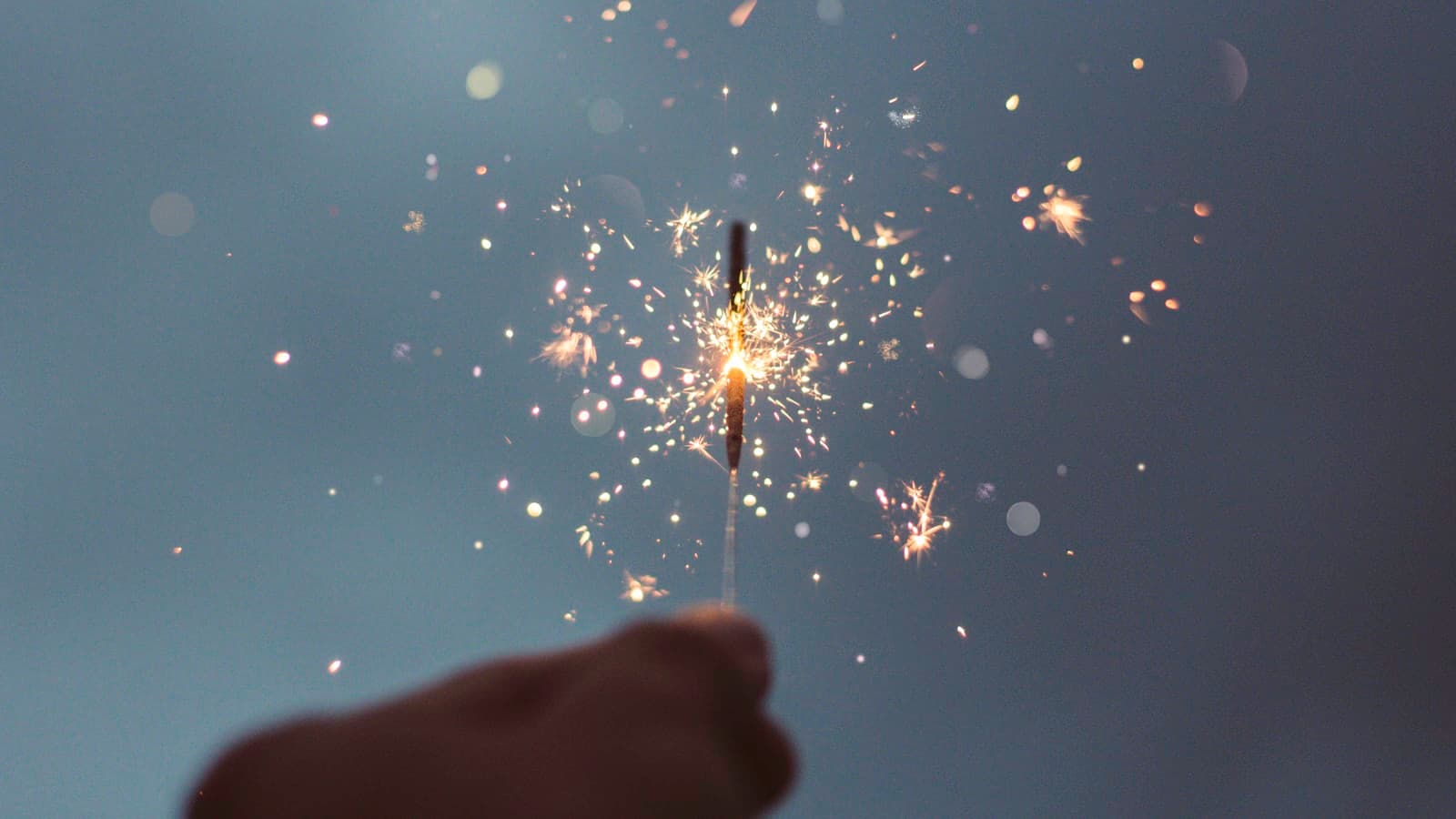 A hand holding a lit sparkler glowing against the dark.