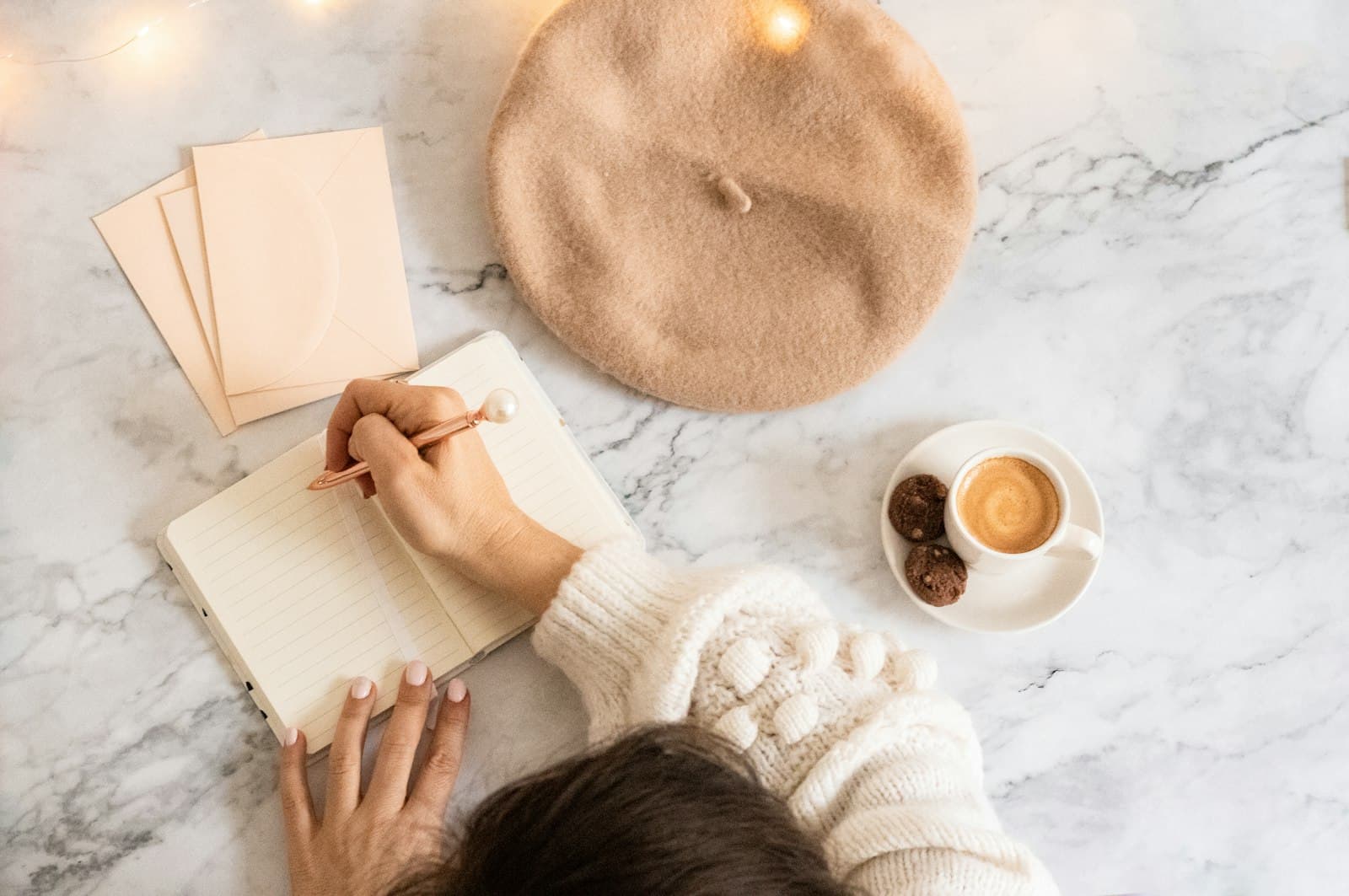 A person writing in a notebook next to a cup of coffee.