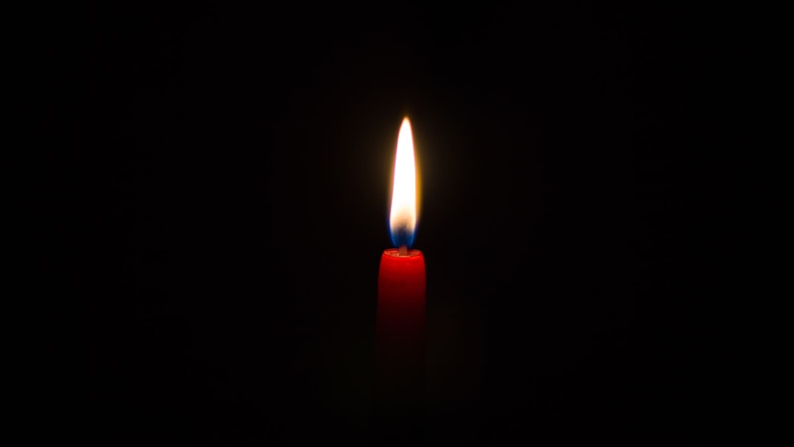 A single red candle burning against a dark background.